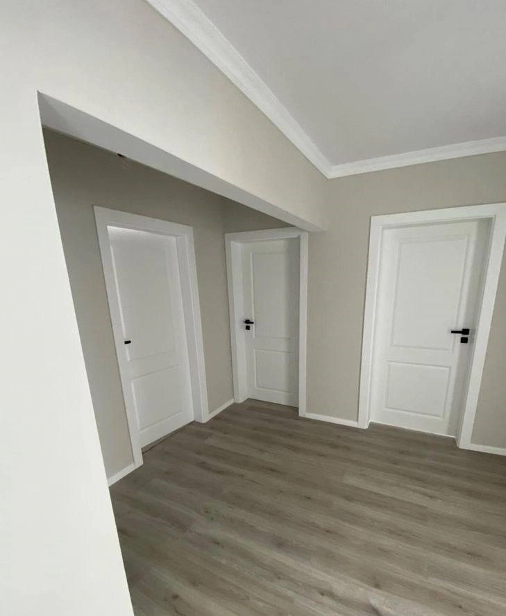 غرفة داخلية بتصميم عصري بجدران بيج وأبواب بيضاء مع أرضية خشبية وتشطيب نظيف وأنيق